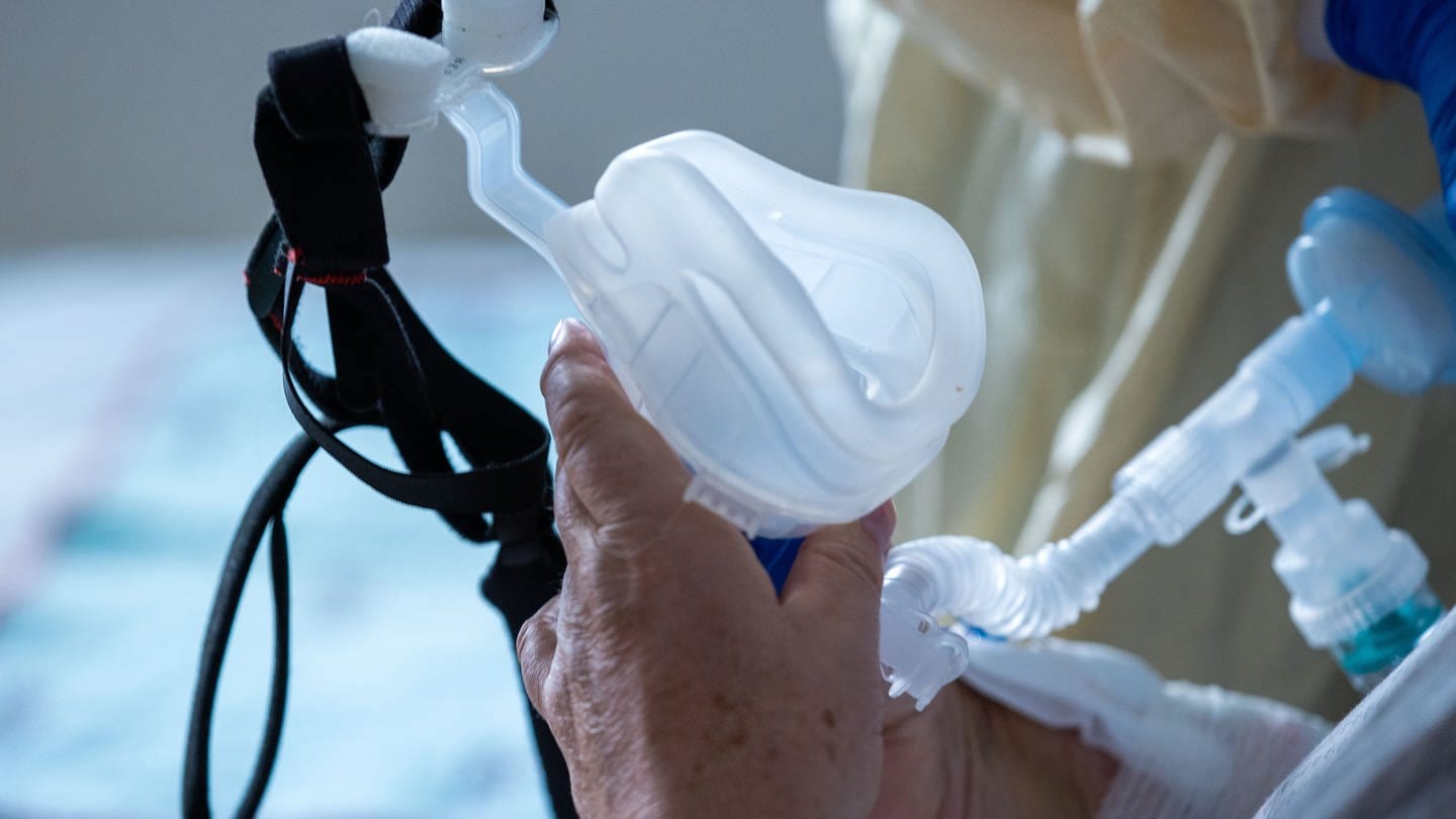 Eine Maske zur Beatmung hält im besonders geschützten Teil der Intensivstation des Universitätsklinikums Greifswald ein Covid-19-Patient in seinen Händen.