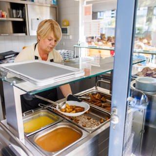 Eine Mitarbeiterin eines Cateringunternehmens schöpft Sauce auf einen Teller mit Kartoffeln und Schnitzel.