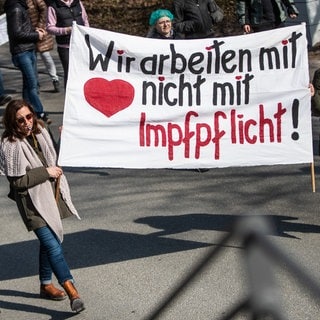 "Wir arbeiten mit Herz, nicht mit Impfpflicht!" steht auf einem Plakat, das Menschen bei einer Demonstration im März gegen die Corona-Maßnahmen der Bundesregierung zeigen.