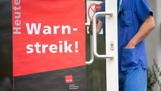 Ein Mitarbeiter des Universitätsklinikums Tübingen geht während eines Warnstreiks an den Uni-Kliniken durch eine Tür mit einem Plakat, auf dem "Heute: Warnstreik!" steht.