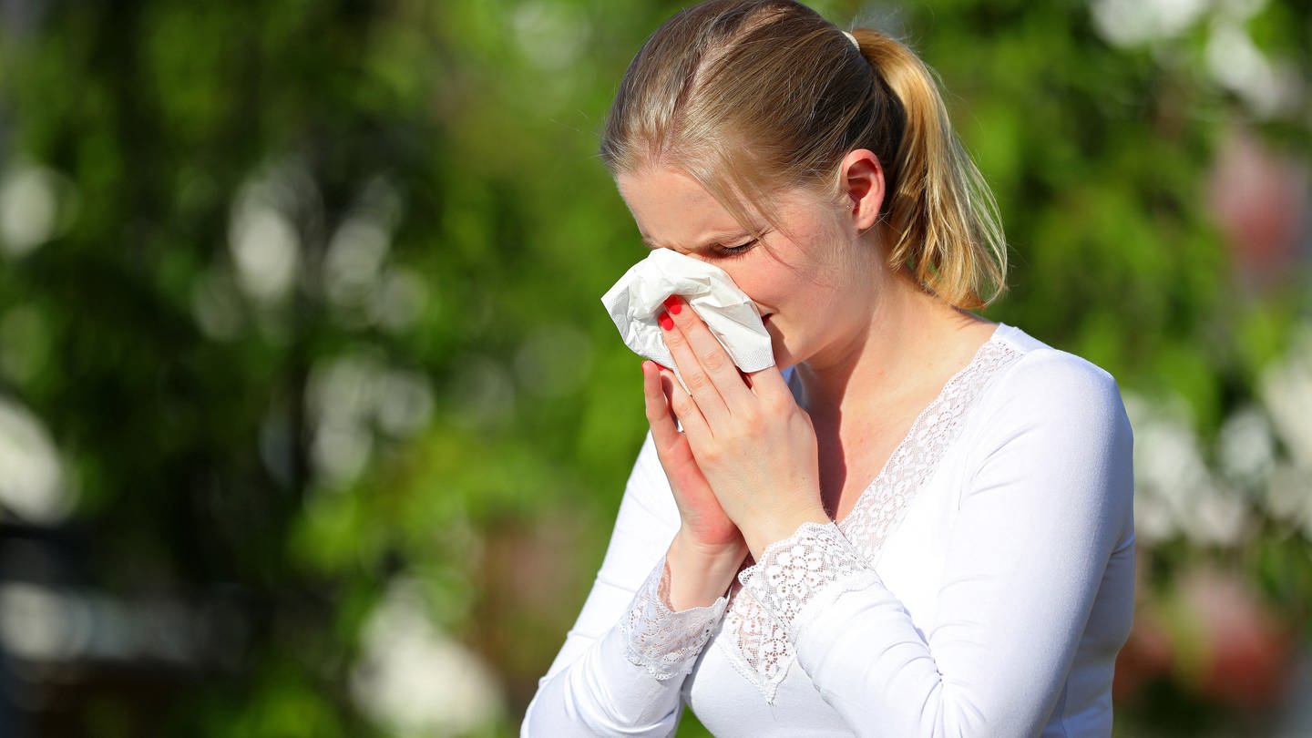 Eine Frau putzt sich im Freien die Nase mit einem Taschentuch