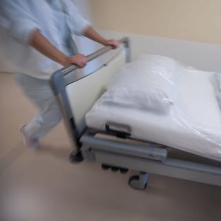 Eine Pflegekarft im Krankenhaus schiebt ein Bett über den Flur.