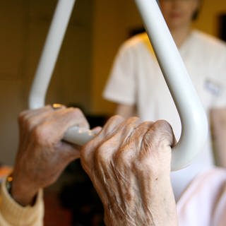Der Eigenanteil für Pflege im Altenheim steigt: Eine Pflegehausbewohnerin hält sich in ihrem Bett an einem Haltegriff fest.
