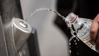 Ein Mann füllt sich an einem Brunnen kostenlos Trinkwasser in die eigene Flasche. 