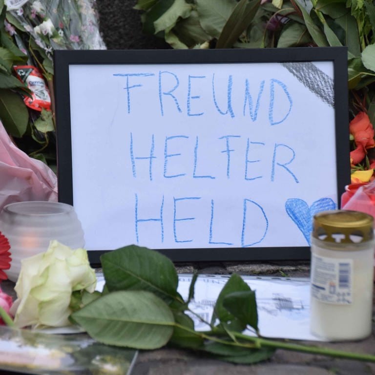 "Freund Helfer Held" ist auf einem schwarz gerahmten Blatt zu lesen, das in unmittelbarer Nähe des Tatorts zusammen mit Blumen und Kerzen niedergelegt wurde.