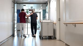 Ein Pfleger geht im Klinikum Stuttgart mit einem Patienten über einen Flur.