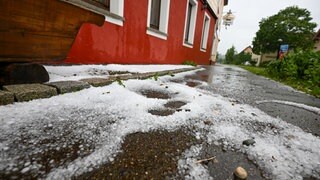 Hagelkörner liegen am Nachmittag auf einem Gehweg vor einem Haus.