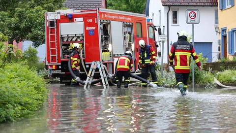 Einsatzkräfte der Feuerwehr im Einsatz nach einem Unwetter mit Starkregen auf einer überfuteten Straße in Veringenstadt (Kreis Sigmaringen)
