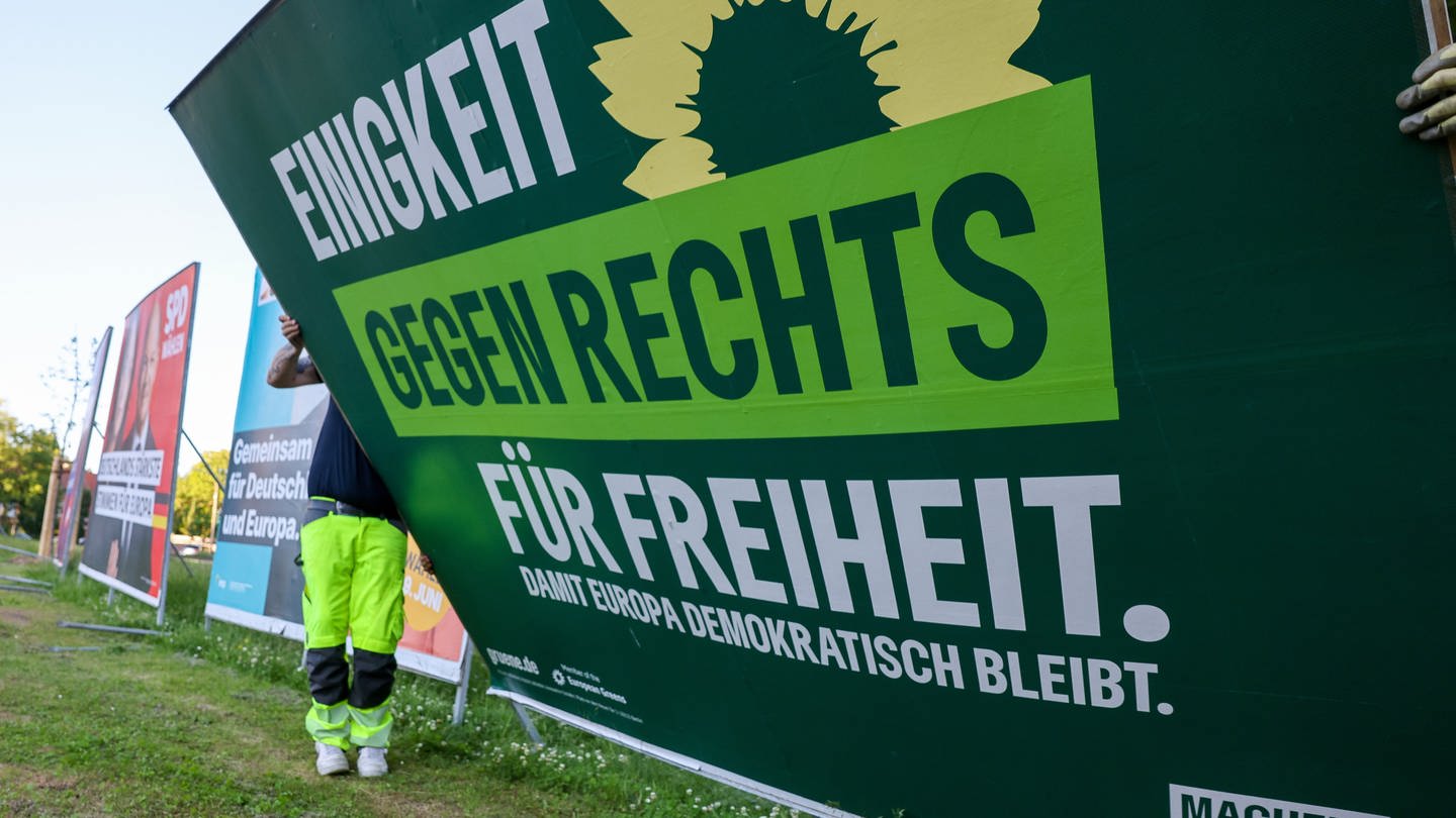 Zwei Mitarbeiter einer Firma für Werbeaufsteller bauen ein Wahlplakat der Partei Bündnis 90/Die Grünen nach der Europawahl ab.