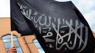  Ein Muslim hält eine islamische Fahne mit dem Glaubensbekenntnis, der sogenannten Schahada in die Höhe (Symbolbild)