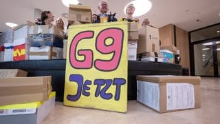 Unterstützer der Elterninitiative "G9 Jetzt! BW" stehen im Foyer des Bürger- und Medienzentrum des Landtags von Baden-Württemberg hinter Kartons, in denen sich Unterschriftenlisten befinden. 