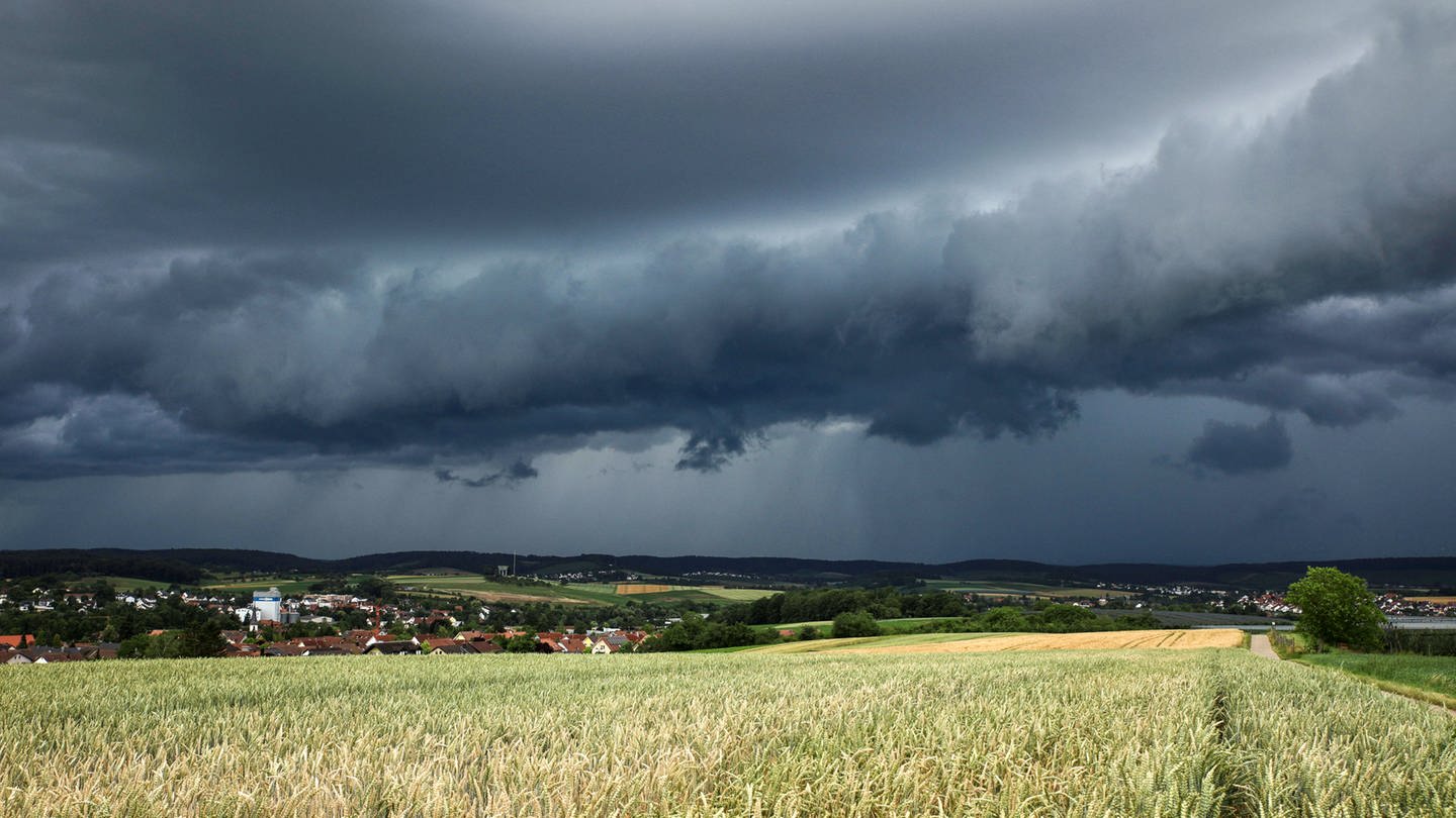 Eine Gewitterzelle mit dunklen Wolken baut sich am Himmel und hinter Feldern nahe Heilbronn auf (Archivbild).