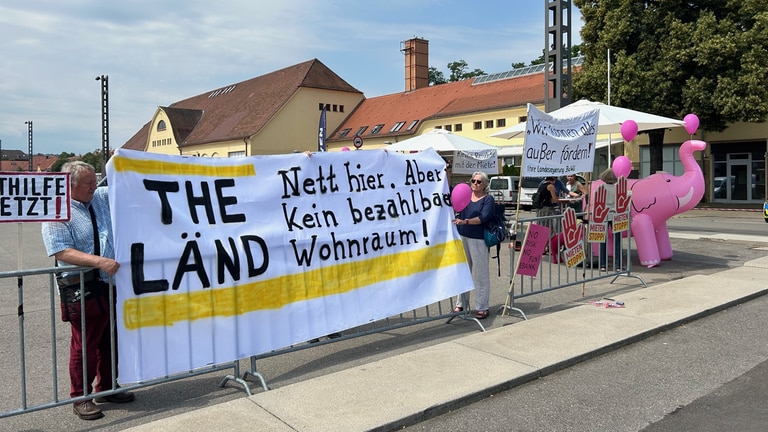 Demonstrierende stehen im Rahmen der Jahresveranstaltung zum Strategiedialog "Bezahlbares Wohnen und innovatives Bauen" mit Plakaten auf einer Straße in Stuttgart