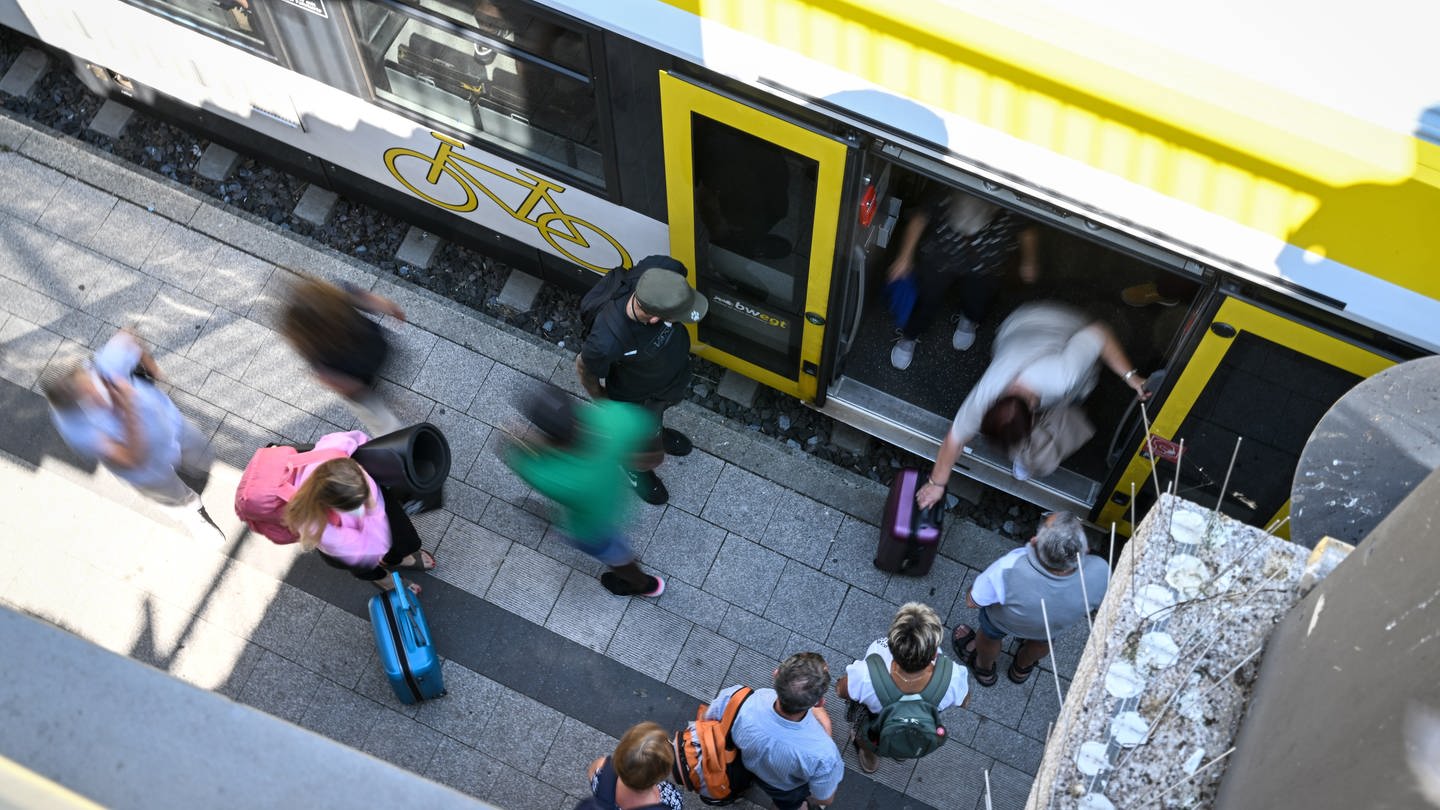 Bild von oben gesehen: Zugreisende stehen am Bahnhof, um in den Zug einzusteigen.