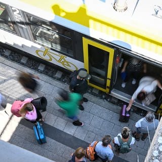 Bild von oben gesehen: Zugreisende stehen am Bahnhof, um in den Zug einzusteigen.