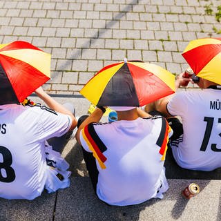EM-Fußballfans sitzend mit Miniatur-Schirmen auf dem Kopf