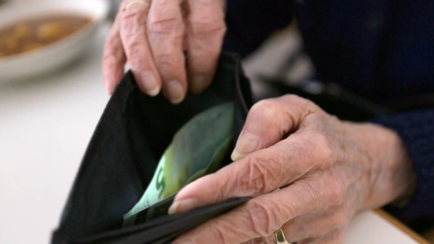 Eine ältere Frau öffnet ihr Portemonnaie, zu sehen sind ihre Hände und ein Fünf-Euro-Schein.