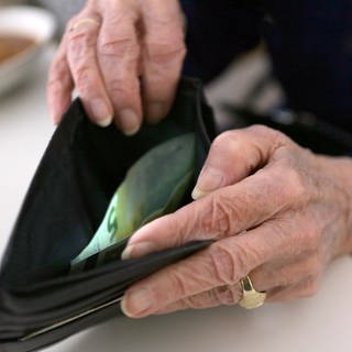 Eine ältere Frau öffnet ihr Portemonnaie, zu sehen sind ihre Hände und ein Fünf-Euro-Schein.