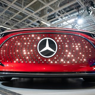 Ein Elektroauto mit leuchtendem Mercedes-Stern steht in einer Halle des Mercedes Benz eCampus.