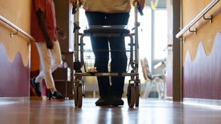 Ein Bewohner eines Pflegeheims geht mit einem Rollator einen Gang entlang.