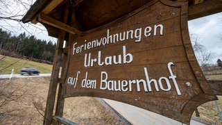 "Ferienwohnungen Urlaub auf dem Bauernhof" steht auf einem Schild an einer Straße.