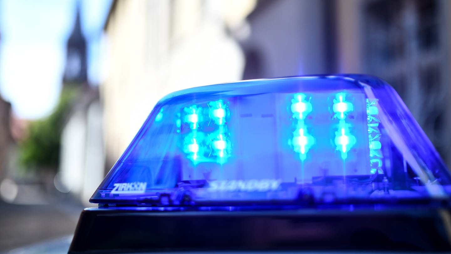 Ein Polizeiauto mit blinkendem Blaulicht steht vor einem Gebäude. Ein zwei Jahre altes Mädchen ist am Samstagvormittag auf einem Supermarktparkplatz in Dornhan (Kreis Rottweil) nach dem Zusammenstoß mit einem Auto noch am Unfallort gestorben. (Symbolbild)