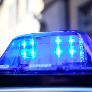 Ein Polizeiauto mit blinkendem Blaulicht steht vor einem Gebäude. Ein zwei Jahre altes Mädchen ist am Samstagvormittag auf einem Supermarktparkplatz in Dornhan (Kreis Rottweil) nach dem Zusammenstoß mit einem Auto noch am Unfallort gestorben. (Symbolbild)