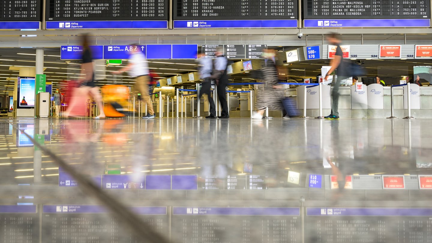 Reisende gehen am Flughafen mit Gepäck durch die Abflughalle. Durch ein fehlerhaftes Software-Update kommt es derzeit zu Flugausfällen in BW.