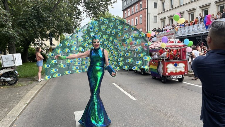 Eine Teilnehmerin des CSD in Stuttgart steht als prächtiger Pfau kostümiert auf einer Straße.