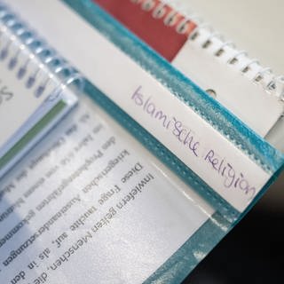 Ein Hefter mit der Aufschrift "Islamische Religion" liegt auf einem Schultisch.