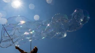 Ein Seifenblasenkünstler fängt auf dem Münsterplatz in Ulm die Sonne ein. In den kommenden Tagen soll es heiß werden.