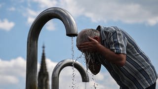Ein Passant kühlt sich an einem Mineralwasserbrunnen ab. In Baden-Württemberg warnt der Deutsche Wetterdienst vor Hitze. 
