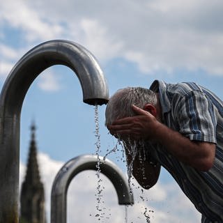 Ein Passant kühlt sich an einem Mineralwasserbrunnen ab. In Baden-Württemberg warnt der Deutsche Wetterdienst vor Hitze. 