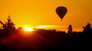 Ein Heißluftballon fährt am Himmel, während neben ihm die Sonne aufgeht.