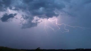 Ein Blitz zuckt bei einem Sommergewitter am abendlichen Himmel (Symbolbild)