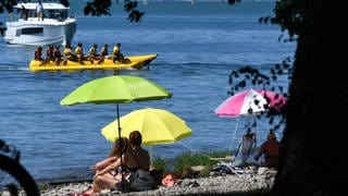 Sonnenhungrige sitzen am sogenannten Malereck unter ihren Sonnenschirmen. Der Sommer lockt viele Gäste in die Touristenhochburgen, etwa an den Bodensee.
