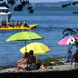 Sonnenhungrige sitzen am sogenannten Malereck unter ihren Sonnenschirmen. Der Sommer lockt viele Gäste in die Touristenhochburgen, etwa an den Bodensee.