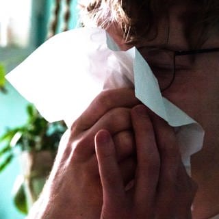 Ein Mann putzt sich mit einem Taschentuch die Nase. (Archivbild)