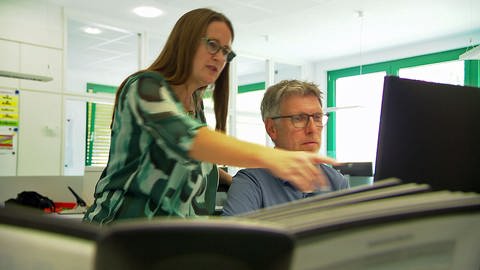 Betriebsleiterin Manuela Lüttke schaut mit einem Kollegen auf einen Monitor.