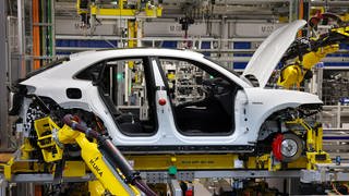 Industrieroboter arbeiten an einem vollelektrischen Porsche Macan nach der Hochzeit (der Verbindung von Fahrwerk und Motor mit der Karosse) im Werk Leipzig. Die Auslastung der Automobilhersteller-Werke war 2023 in Deutschland deutlich zurückgegangen.