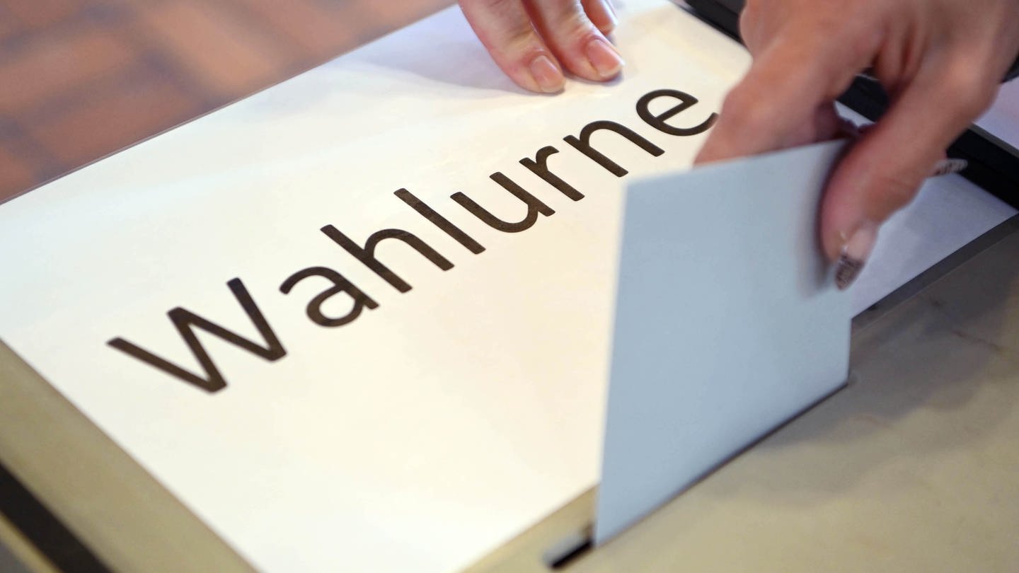 In einem Wahllokal wird ein Stimmzettel in eine Wahlurne geworfen.