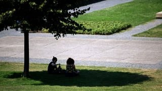 Zwei Personen sitzen in der Innenstadt von Stuttgart im Schatten unter einem Baum.