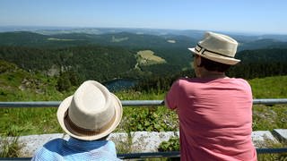 Zwei Touristen mit Strohhüten betrachten auf dem Gipfel des Feldbergs im Schwarzwald das Panorama. 2024 haben die Gäste- und Übernachtungszahlen in Baden-Württemberg weiter zugenommen.