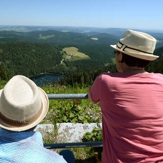 Zwei Touristen mit Strohhüten betrachten auf dem Gipfel des Feldbergs im Schwarzwald das Panorama. 2024 haben die Gäste- und Übernachtungszahlen in Baden-Württemberg weiter zugenommen.