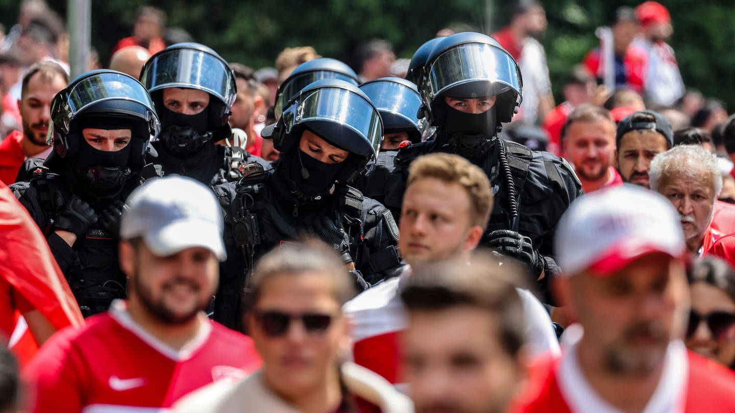 Ein Fanmarsch wird von der Polizei Polizisten in Schutzausrüstung begleitet.