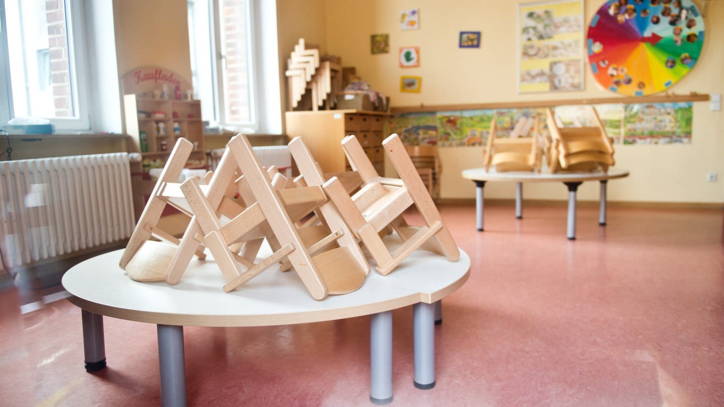 Hochgestellte Stühle stehen am in Stuttgar hinter einem Fenster in einer Kindertagesstätte.