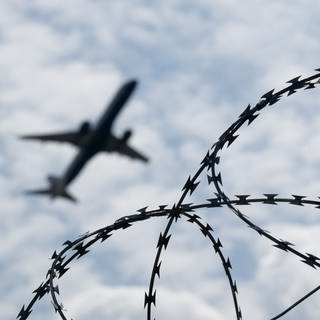 Ein Flugzeug hebt an einem Flughafen hinter einem Zaun mit Natodraht ab.