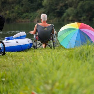 Ein Mann sitzt in einem Campingstuhl an einem Badesee.