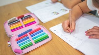 Ein Grundschüler und eine Grundschülerin sitzen in einem Wohnzimmer am Tisch und erledigen Schulaufgaben. In Baden-Württemberg beginnt am 9. September wieder die Schule.