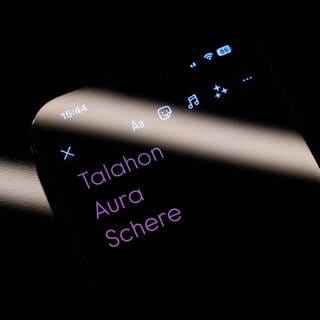 Die drei Worte "Talahon", "Aura" und "Schere" sind auf dem Display eines Smartphones zu sehen.